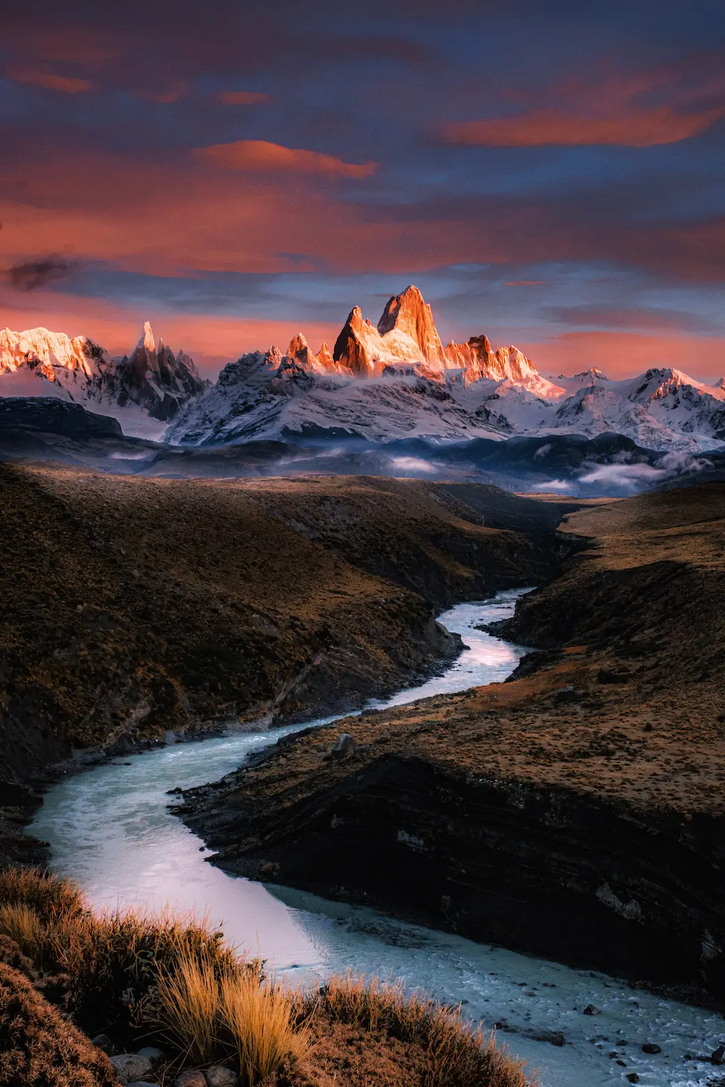 A scene of a river meandering from the iconic El Chalten mountain range unfolds at sunrise