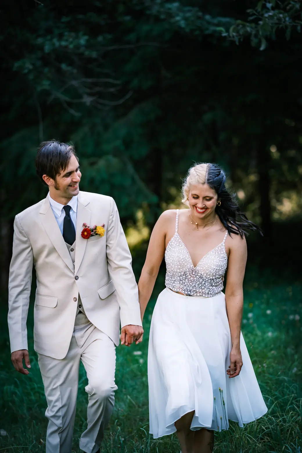 A couple holding hands during a summer wedding strolls through a field