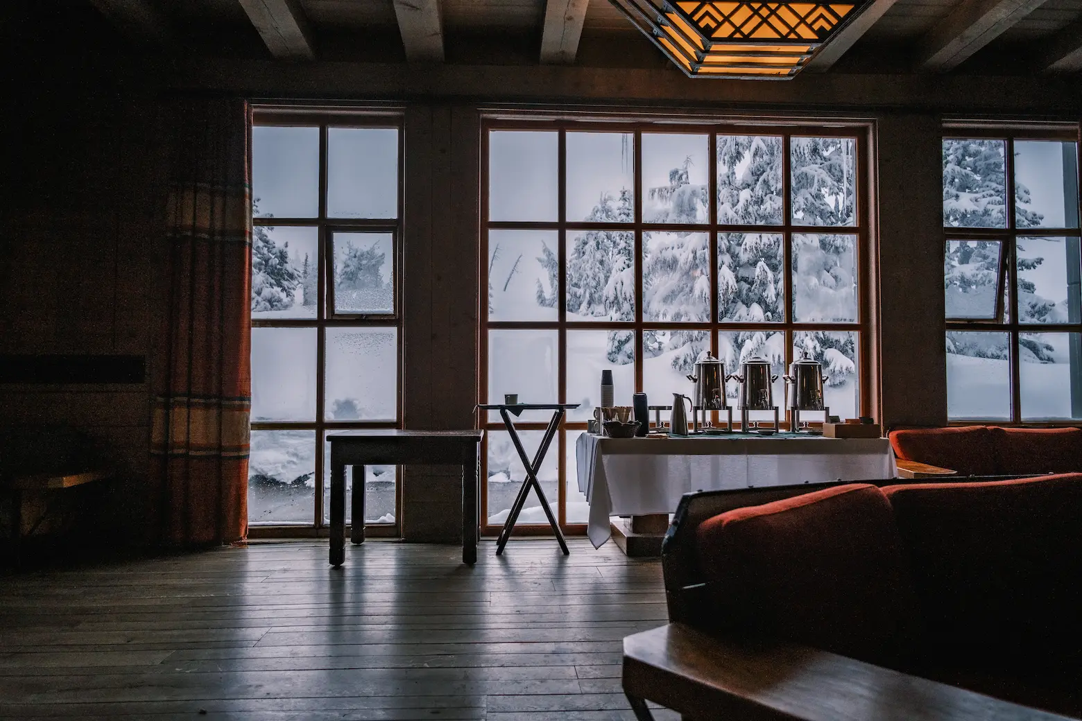 The picture shows a point-of-view angle of looking at a large set of windows with snow outside and coffee dispensers on a table